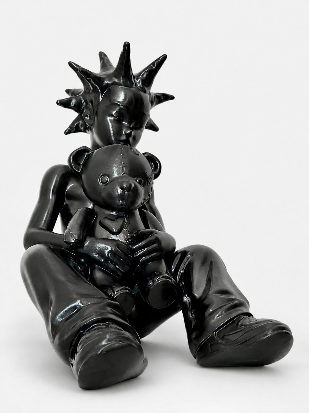 Black sculpture of a figure holding a teddy bear on a white background